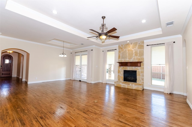 unfurnished living room with arched walkways, visible vents, a tray ceiling, and wood finished floors