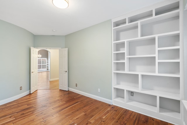 unfurnished bedroom with arched walkways, baseboards, and hardwood / wood-style floors