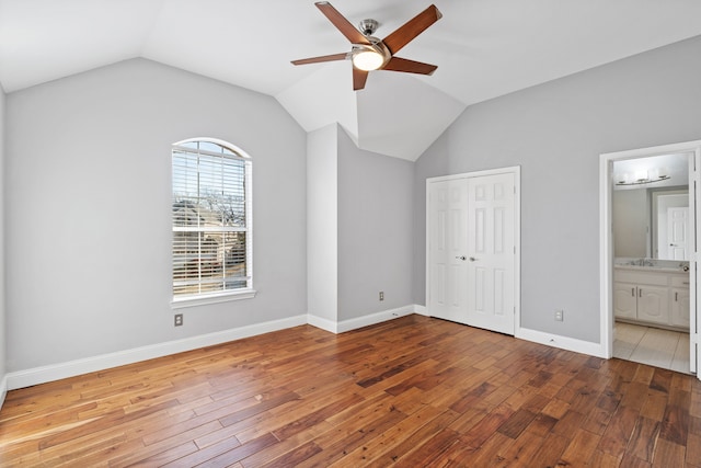 unfurnished bedroom with connected bathroom, hardwood / wood-style flooring, baseboards, vaulted ceiling, and a closet