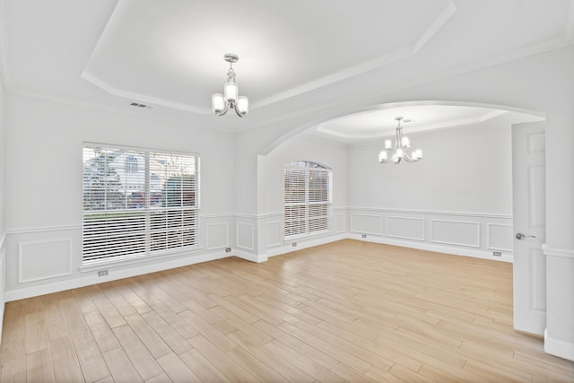 spare room featuring a chandelier, light wood-style flooring, a raised ceiling, and visible vents