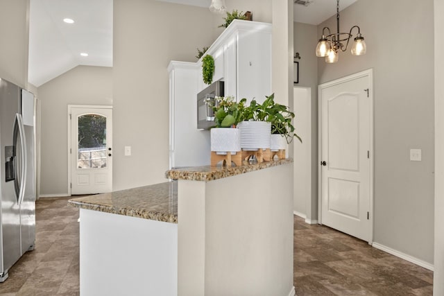 kitchen with white cabinets, vaulted ceiling, dark stone countertops, stainless steel fridge, and a peninsula