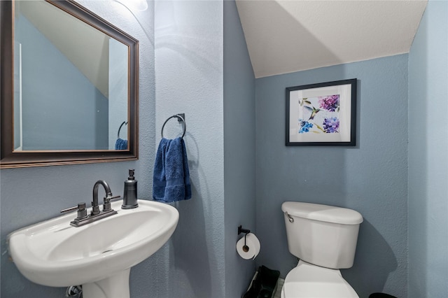 half bath featuring vaulted ceiling, a textured wall, a sink, and toilet