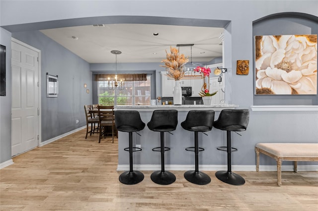 kitchen with a notable chandelier, a kitchen bar, light wood-type flooring, black microwave, and baseboards