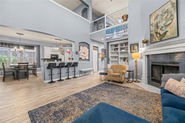 living area featuring built in features, a notable chandelier, a tiled fireplace, wood finished floors, and baseboards