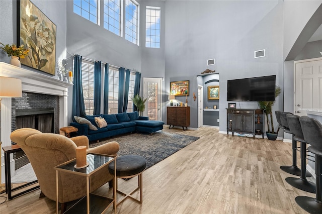 living room featuring wood finished floors, a tile fireplace, visible vents, and baseboards