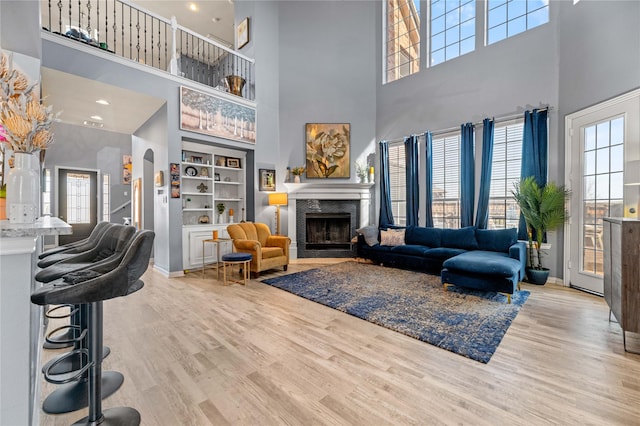 living room with baseboards, arched walkways, a premium fireplace, wood finished floors, and built in shelves