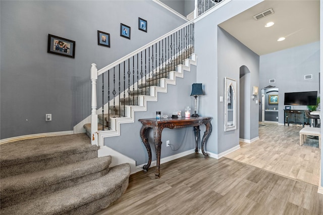 stairway with arched walkways, visible vents, a high ceiling, and wood finished floors