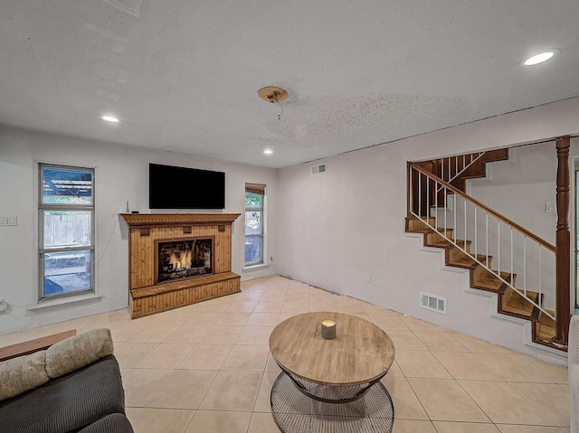 living area featuring light tile patterned floors, visible vents, stairway, a healthy amount of sunlight, and a lit fireplace