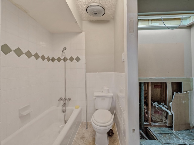 bathroom featuring a textured ceiling, bathtub / shower combination, toilet, a wainscoted wall, and tile walls