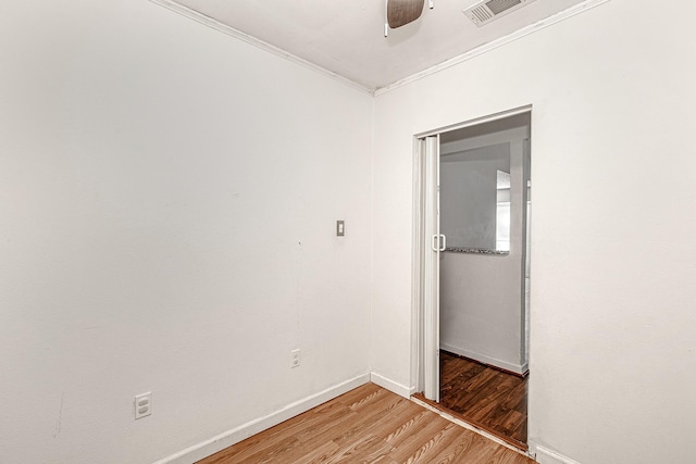 empty room with visible vents, light wood-style flooring, a ceiling fan, crown molding, and baseboards