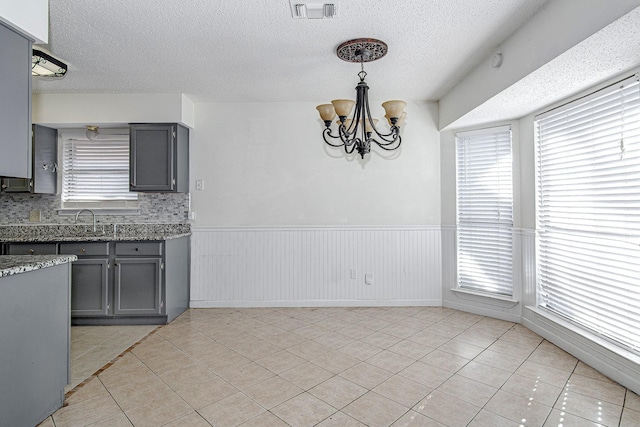 unfurnished dining area featuring a wainscoted wall, an inviting chandelier, light tile patterned floors, and visible vents