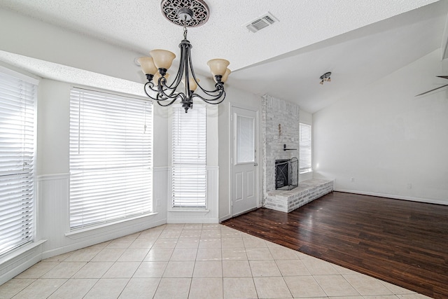 unfurnished dining area featuring tile patterned flooring, visible vents, a brick fireplace, vaulted ceiling, and a notable chandelier