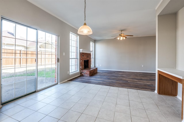 unfurnished living room with light tile patterned floors, a brick fireplace, a wealth of natural light, and crown molding