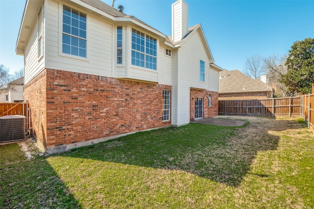 back of property with central AC unit, a fenced backyard, brick siding, a lawn, and a chimney