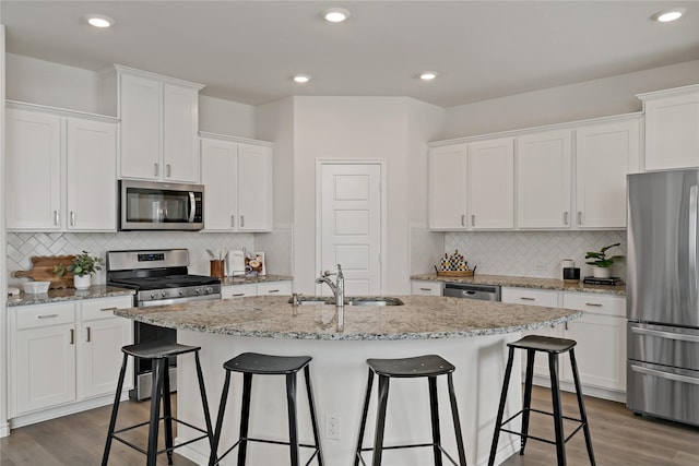 kitchen featuring stainless steel appliances, a sink, white cabinets, dark wood-style floors, and a center island with sink