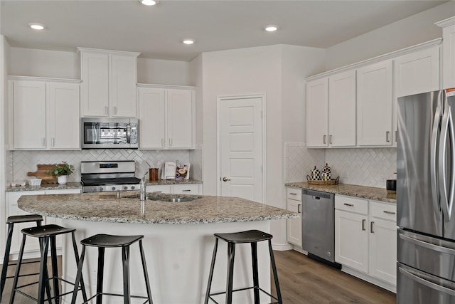 kitchen featuring stainless steel appliances, dark wood-type flooring, white cabinets, a sink, and a kitchen bar