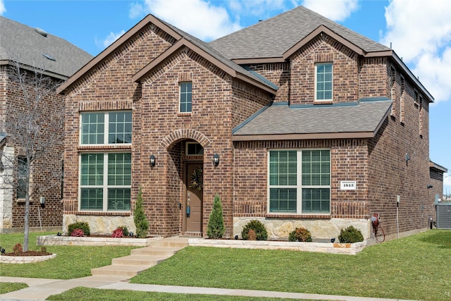 view of front of home featuring a shingled roof, a front lawn, and brick siding