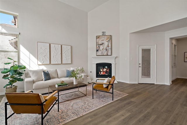 living room with a towering ceiling, baseboards, wood finished floors, and a glass covered fireplace