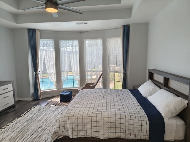 bedroom with baseboards, visible vents, a raised ceiling, and wood finished floors