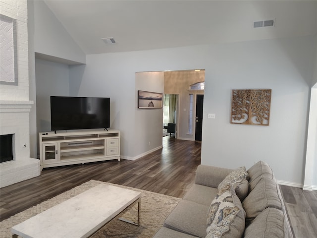 living room with lofted ceiling, a brick fireplace, visible vents, and wood finished floors