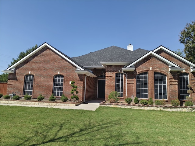 view of front of property with roof with shingles, a front lawn, a chimney, and brick siding