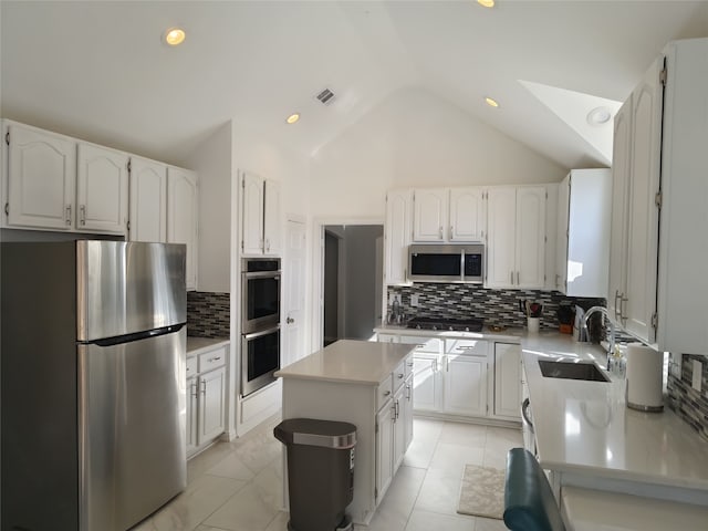 kitchen featuring lofted ceiling, appliances with stainless steel finishes, a sink, and white cabinetry