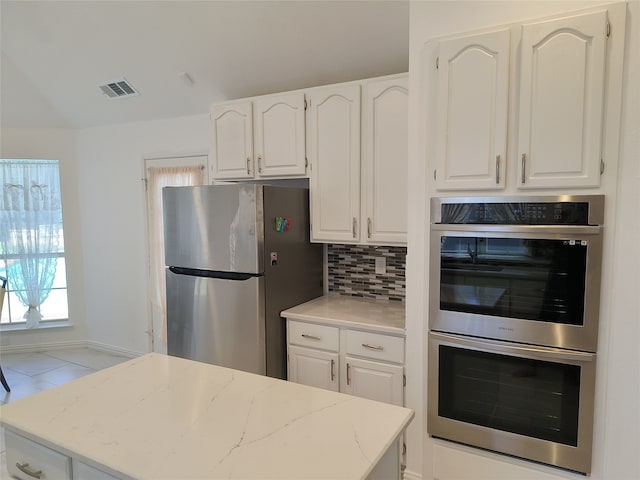 kitchen featuring appliances with stainless steel finishes, white cabinets, backsplash, and light stone counters