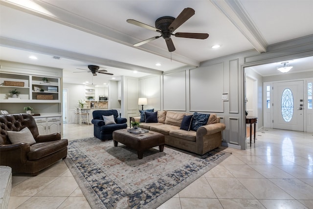 living area with light tile patterned floors, ceiling fan, a decorative wall, ornamental molding, and beam ceiling