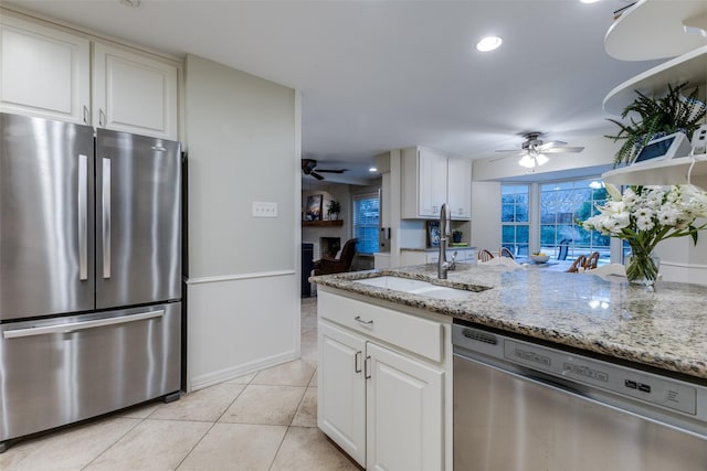 kitchen featuring stainless steel appliances, light tile patterned flooring, a sink, white cabinetry, and light stone countertops