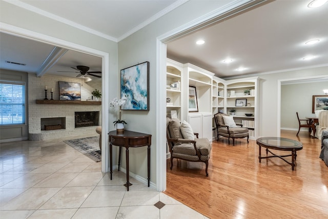 living area with light tile patterned floors, baseboards, ceiling fan, ornamental molding, and a fireplace