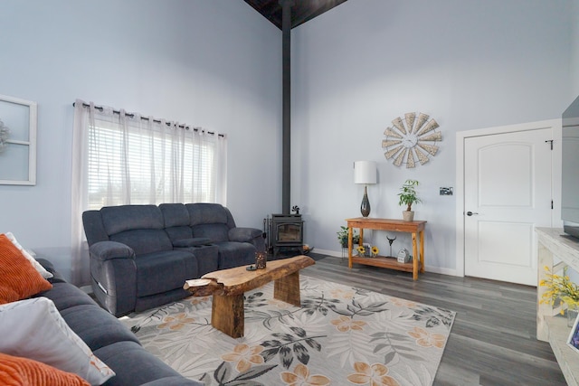 living room featuring a high ceiling, wood finished floors, a wood stove, and baseboards