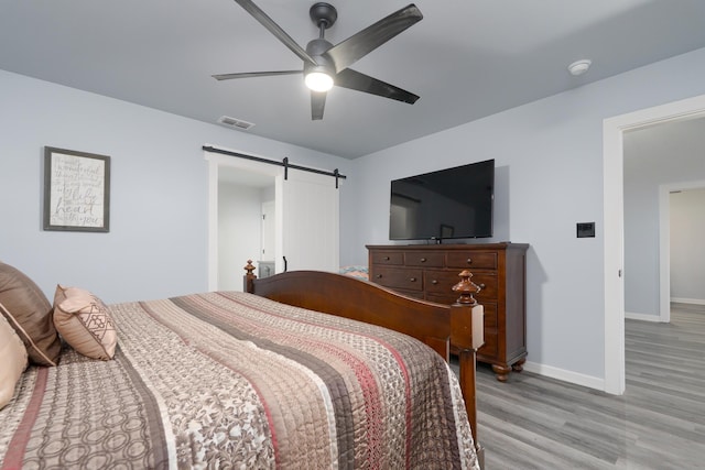 bedroom with visible vents, light wood-style flooring, a barn door, ceiling fan, and baseboards