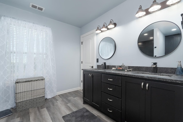 full bath with double vanity, baseboards, visible vents, wood finished floors, and a sink