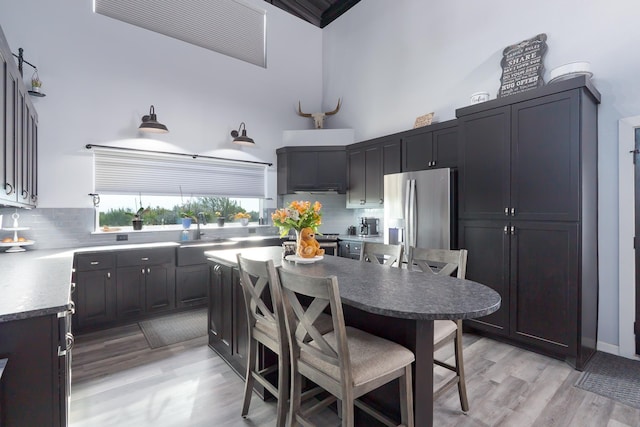 kitchen with decorative backsplash, a high ceiling, a kitchen bar, stainless steel refrigerator with ice dispenser, and a sink