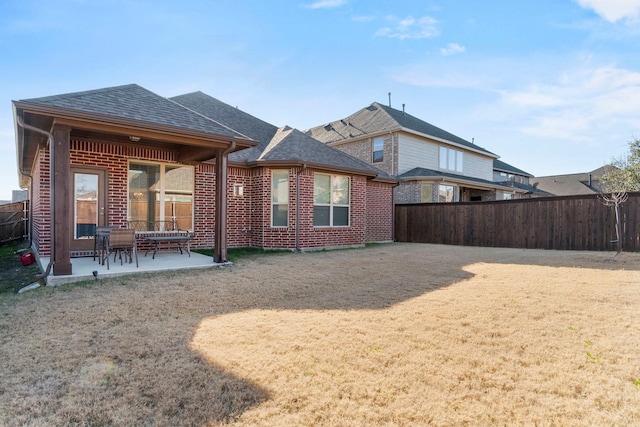 rear view of property featuring a patio, roof with shingles, fence, a yard, and brick siding