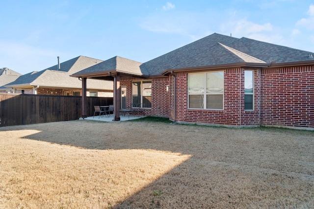 rear view of property with a shingled roof, fence, a patio, and brick siding