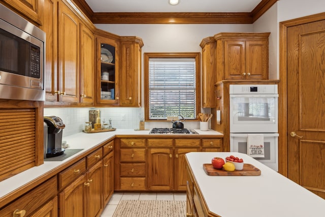 kitchen featuring tasteful backsplash, light countertops, appliances with stainless steel finishes, brown cabinetry, and light tile patterned flooring