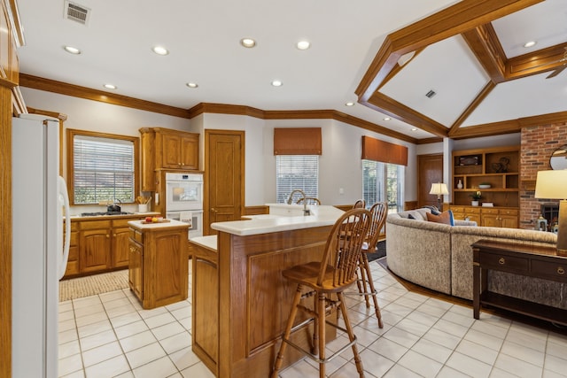 kitchen with white appliances, light tile patterned floors, visible vents, a kitchen island with sink, and light countertops