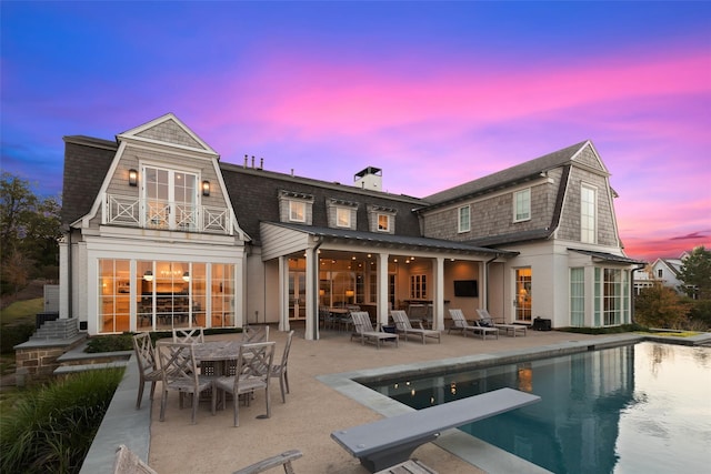 back of house with a balcony, outdoor dining area, an outdoor pool, a chimney, and a patio area