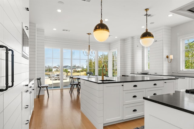 kitchen with a sink, visible vents, white cabinets, light wood-style floors, and dark countertops