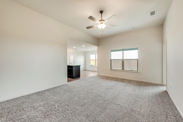 unfurnished living room featuring a ceiling fan, light colored carpet, visible vents, and baseboards