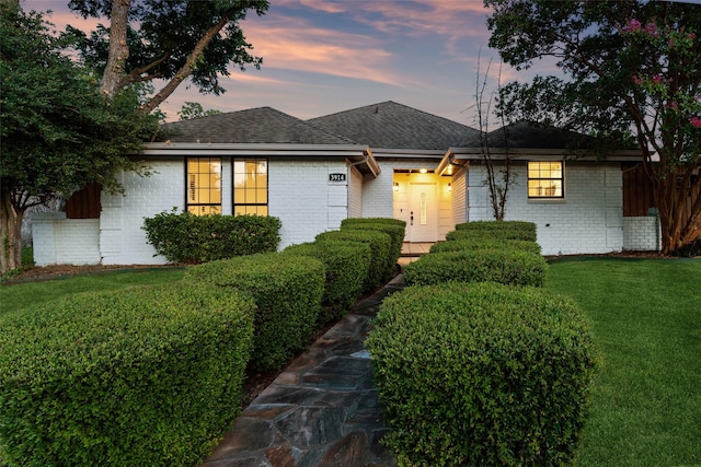 ranch-style house with a shingled roof, brick siding, and a yard