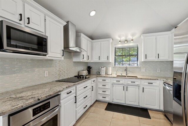 kitchen featuring stainless steel appliances, a sink, white cabinets, vaulted ceiling, and wall chimney exhaust hood