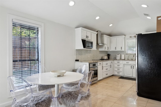 kitchen featuring stainless steel appliances, lofted ceiling, decorative backsplash, white cabinets, and wall chimney exhaust hood