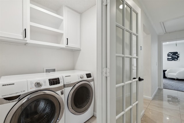 clothes washing area featuring cabinet space, attic access, baseboards, and washer and dryer