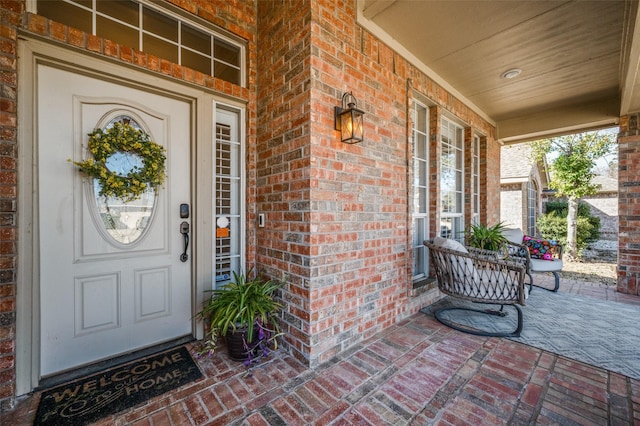 doorway to property featuring a porch and brick siding