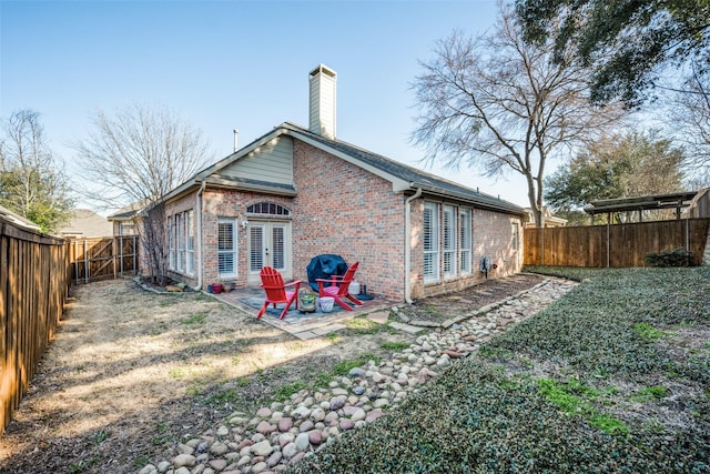 back of property featuring a fenced backyard, a chimney, a patio, and brick siding