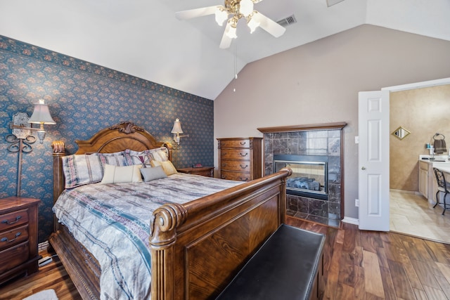 bedroom with wallpapered walls, visible vents, vaulted ceiling, and wood finished floors