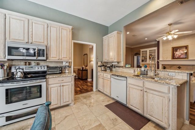 kitchen with stainless steel appliances, a peninsula, a sink, light stone countertops, and tasteful backsplash