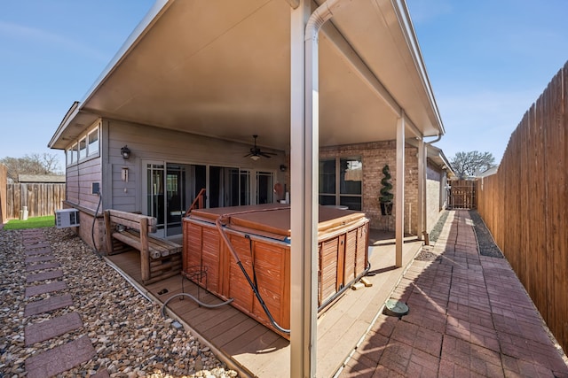 back of property with a hot tub, ceiling fan, a fenced backyard, a patio, and brick siding